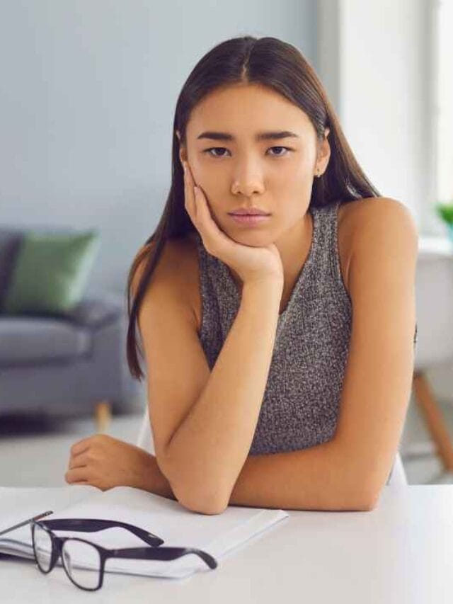 Mulher com expressão de frustração sentada em escritório, com materiais de trabalho à sua frente, sugerindo bloqueio criativo causado por ambiente barulhento.