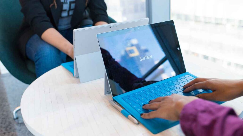 Duas pessoas trabalham concentradas em notebooks em uma sala corporativa iluminada, com janelas amplas ao fundo, transmitindo um ambiente tranquilo e silencioso, ideal para produtividade com conforto acústico.