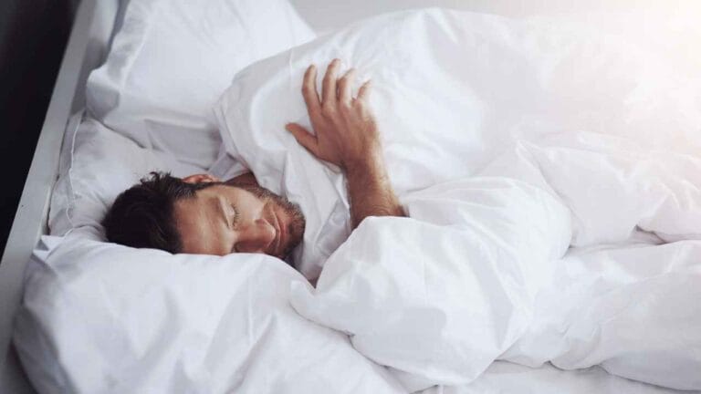 Homem dormindo profundamente em uma cama com lençóis brancos, representando as fases do sono.