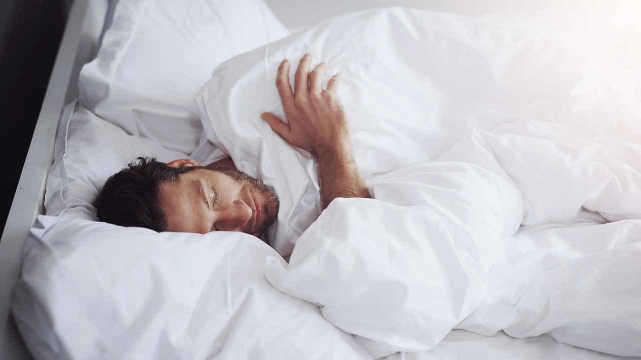 Homem dormindo profundamente em uma cama com lençóis brancos, representando as fases do sono.