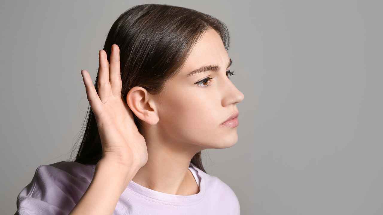 Jovem com expressão atenta segura a mão próxima ao ouvido, simbolizando uma pessoa surda ou com deficiência auditiva.