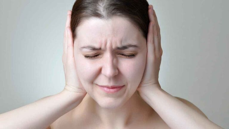Mulher com expressão de incômodo cobrindo os ouvidos com as mãos, simbolizando a sensibilidade e o desconforto causados por ruídos do dia a dia