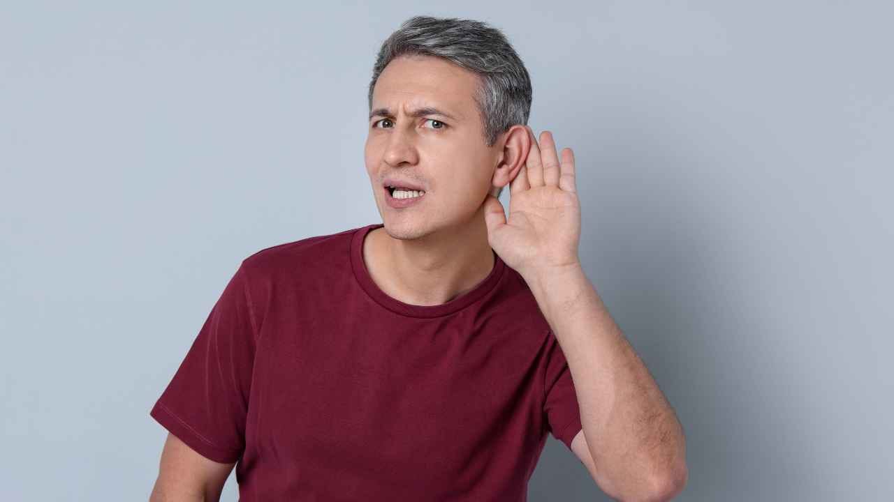 Homem com expressão de incomodo por não conseguir ouvir. Ele está com a mão atrás da orelha.