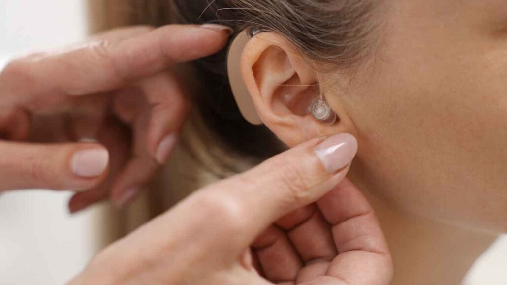 Mãos de mulher ajustando aparelho auditivo em outra pessoa.