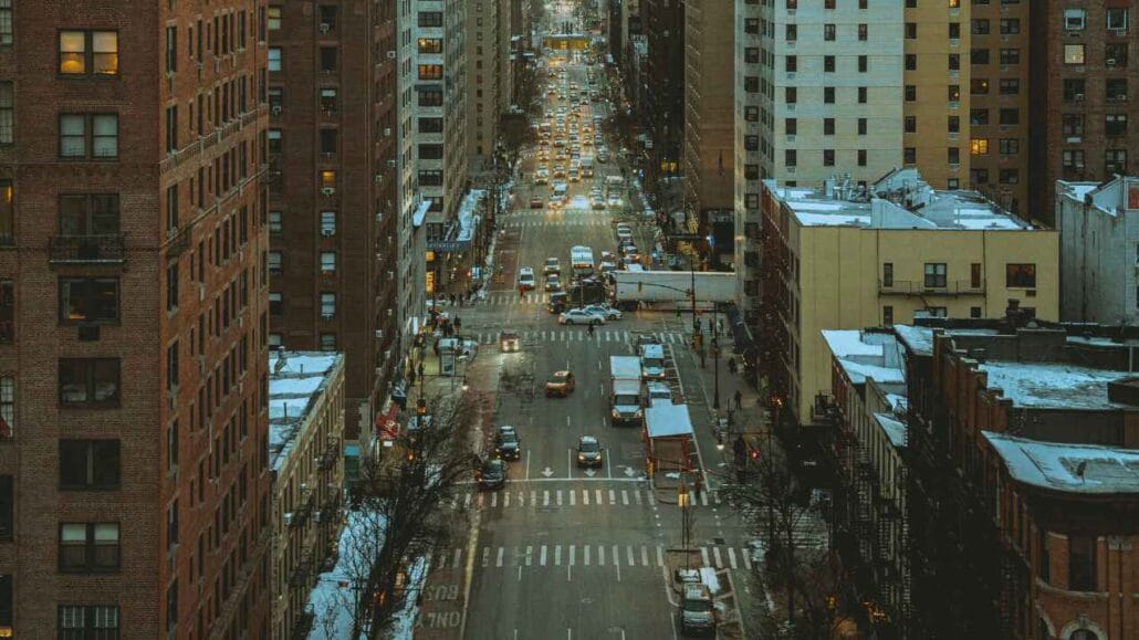 Vista aérea de uma rua movimentada cercada por prédios altos, com tráfego intenso de carros e pedestres, representando o ruído constante