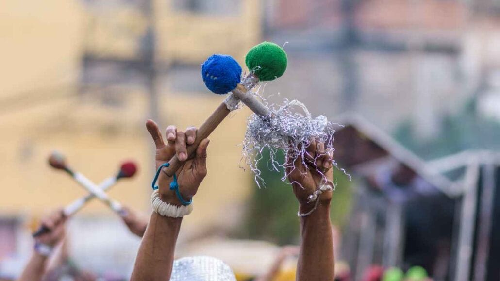 Mãos levantadas segurando instrumentos de percussão coloridos