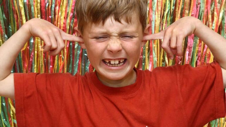 Criança com expressão de incômodo tapa os ouvidos diante de sons altos