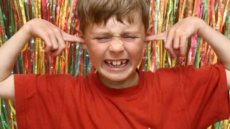 Criança com expressão de incômodo tapa os ouvidos diante de sons altos