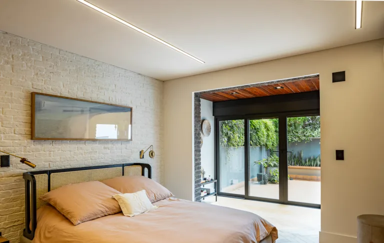 Quarto moderno e aconchegante com cama de casal e ampla porta de vidro voltada para área externa, representando ambiente residencial com conforto e tranquilidade acústica.