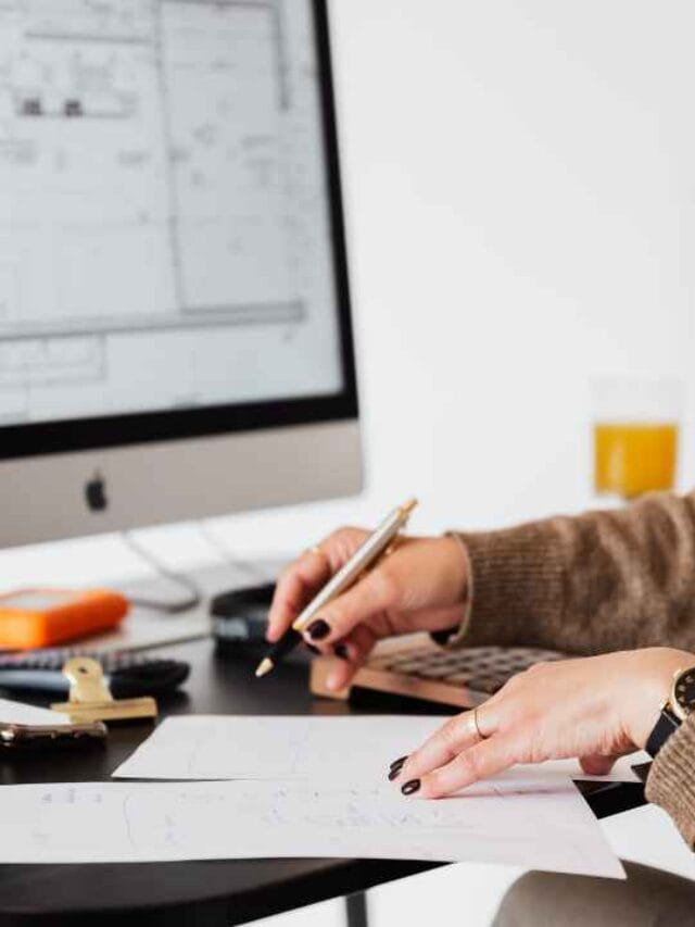 profissional analisando projetos arquitetônicos em computador e documentos impressos