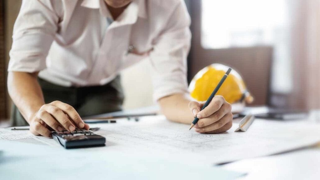 Engenheiro realiza cálculos em uma calculadora enquanto anota informações em uma planta de construção