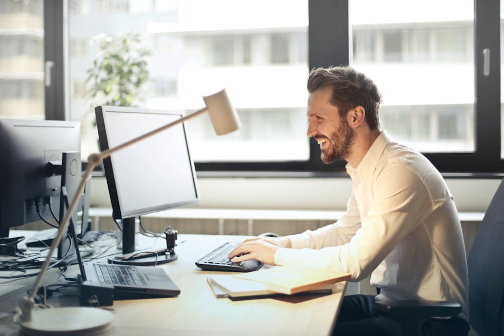 Homem sorridente e concentrado trabalhando em frente ao computador em um ambiente silencioso, com janelas fechadas ao fundo. Representa os benefícios da janela antirruído na concentração de pessoas com TDAH.
Foto por Andrea Piacquadio