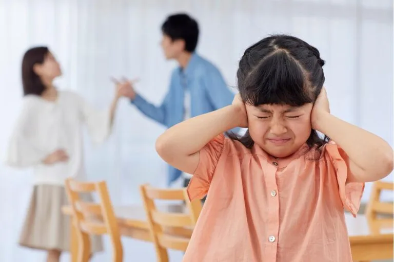 garota tapando os ouvidos com pais atrás