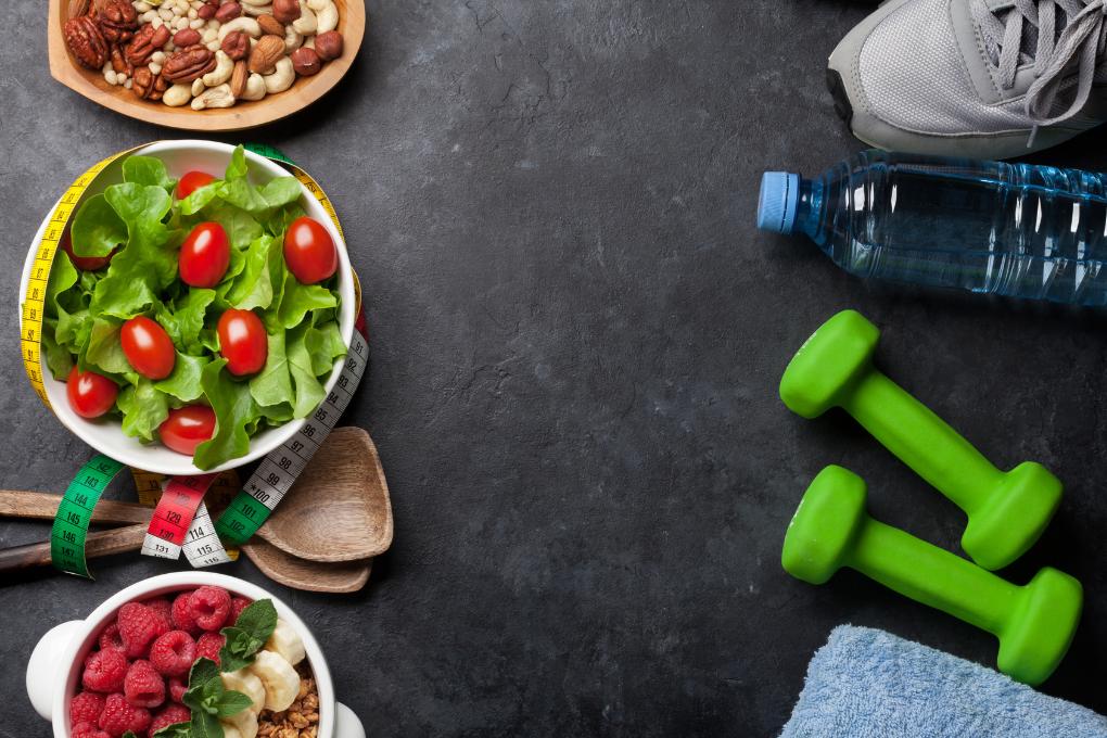 Salada e comidas saudáveis de um lado acompanhadas por uma garrafa de água e pesos para representar saúde
