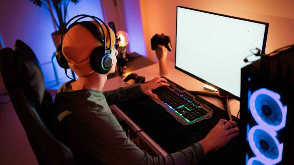 Gamer com fone de ouvido e touca inicia uma stream em ambiente silencioso e iluminado por LEDs, sentado diante de monitor com tela clara e gabinete com ventoinhas azuis, transmitindo de forma concentrada e sem ruídos externos.