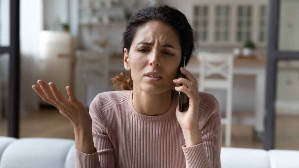 Mulher de expressão séria segura o telefone enquanto faz gesto de indignação com a mão, simbolizando uma situação de denúncia ou reclamação de barulho.