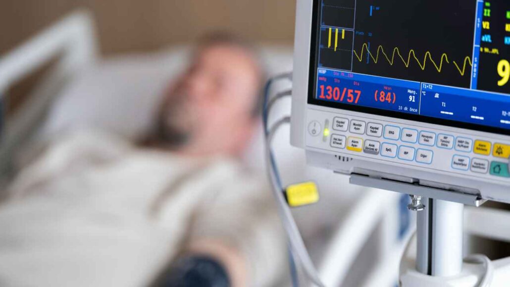 Monitor hospitalar exibindo sinais vitais enquanto paciente permanece deitado em leito de consultorio