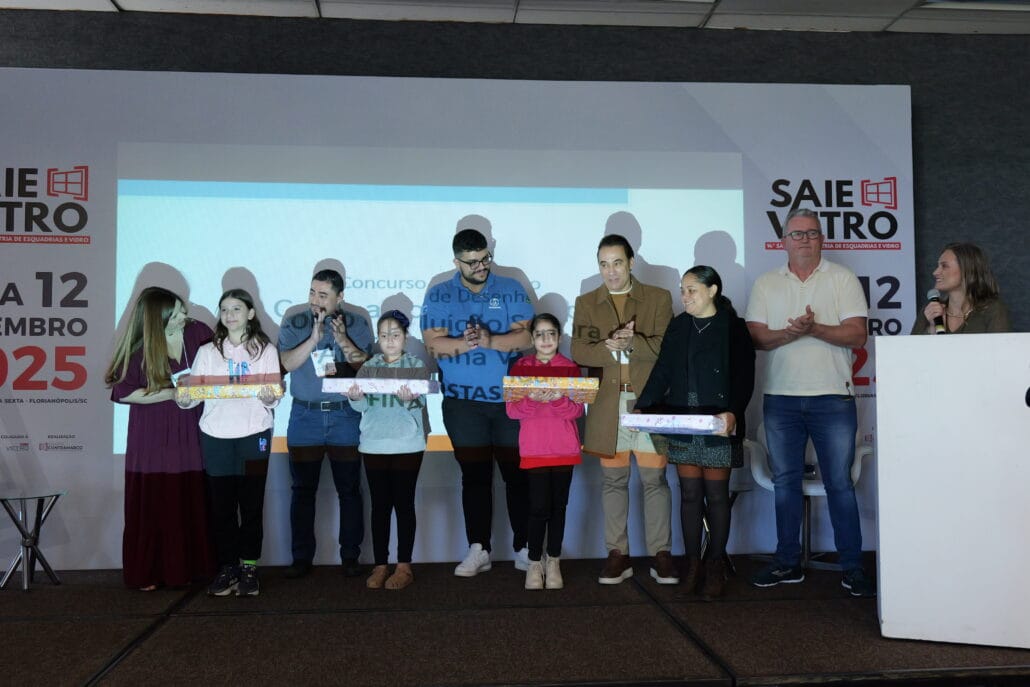 Momento de premiação das alunas finalistas do concurso de desenho promovido pela VidroSom. As crianças estão no palco segurando seus prêmios.