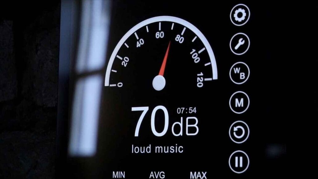 Imagem de um medidor digital exibindo 70 decibéis, indicado como “loud music”, com escala semicircular marcando níveis de 0 a 120 dB, representando a medição de ruído ambiente.