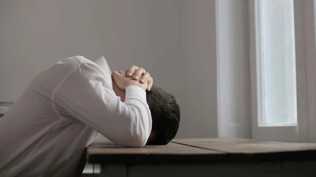 Pessoa com a cabeça apoiada na mesa demonstrando estresse extremo causado pela exposição a altos níveis de ruído e decibéis no ambiente.