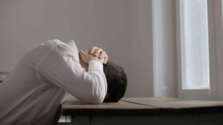 Pessoa com a cabeça apoiada na mesa demonstrando estresse extremo causado pela exposição a altos níveis de ruído e decibéis no ambiente.