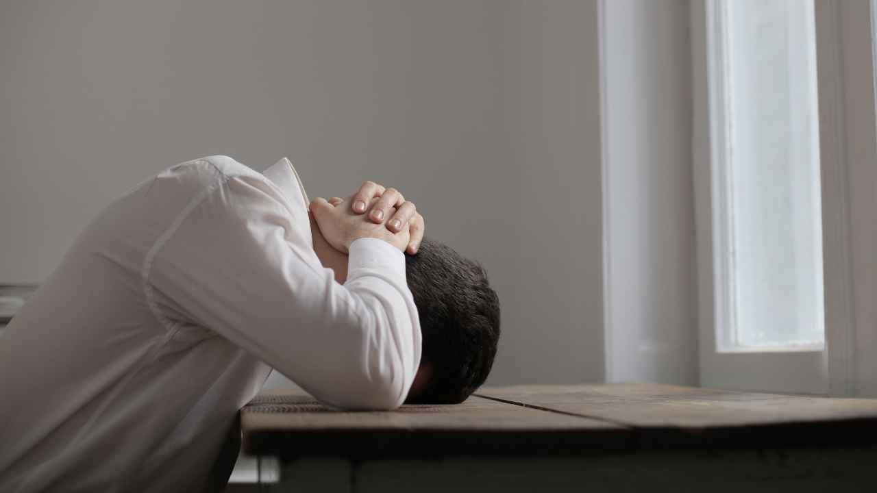 Pessoa com a cabeça apoiada na mesa demonstrando estresse extremo causado pela exposição a altos níveis de ruído e decibéis no ambiente.