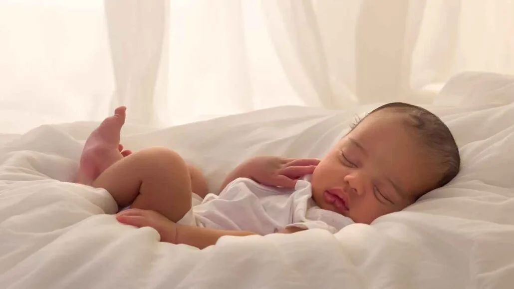 Bebê dormindo tranquilamente deitado em cama com lençóis brancos e iluminação suave perto de uma janela antirruido