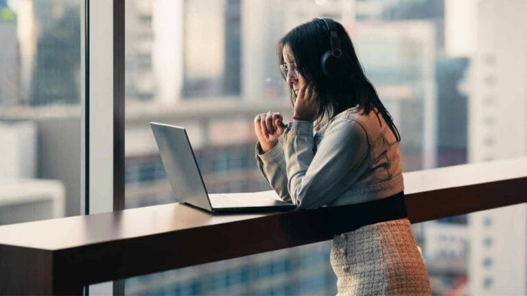 Mulher usando fones de ouvido enquanto trabalha em um notebook próximo à janela