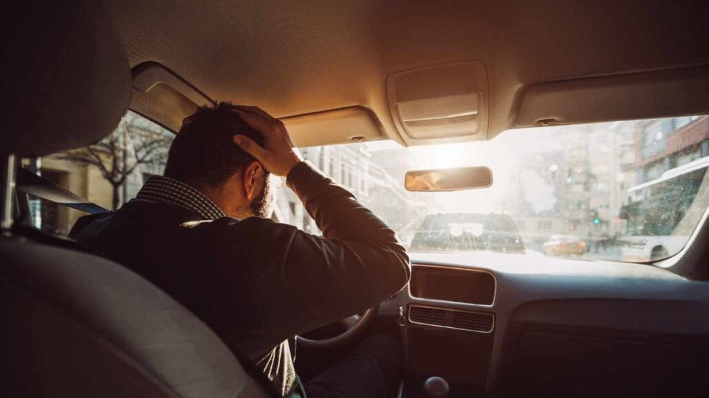 Homem dentro do carro segura a cabeça com uma das mãos