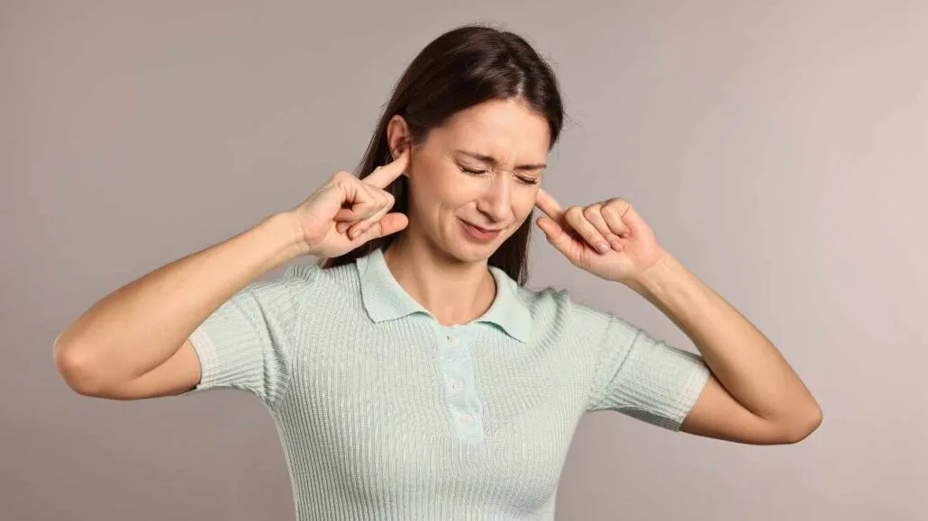 Mulher tampando os ouvidos com expressão de incômodo, representando desconforto causado por ruídos altos ou poluição sonora.