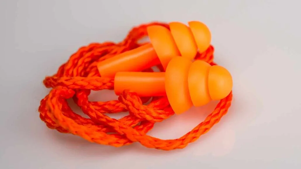 Par de protetores auriculares laranja com cordão, posicionados sobre fundo claro