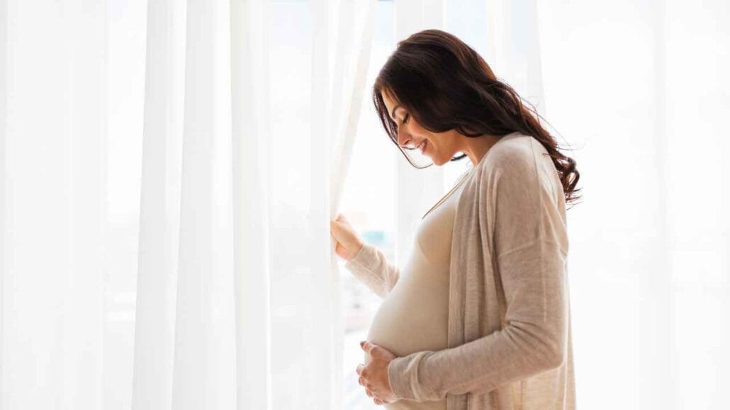 Mulher grávida próxima à janela antirruído segurando a barriga