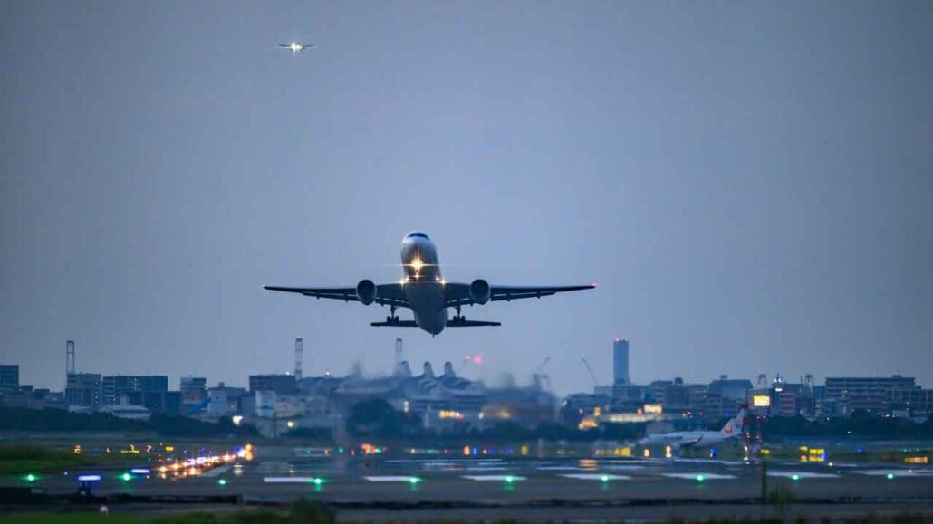 Avião em decolagem canva. Ao fundo uma cidade ao anoitecer.
