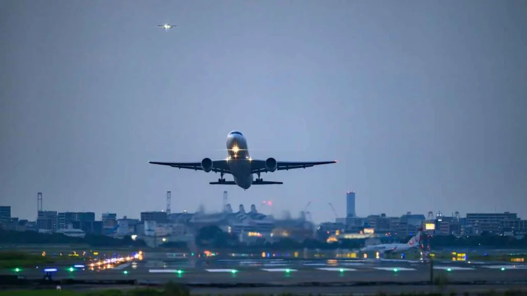 Avião em decolagem canva. Ao fundo uma cidade ao anoitecer.