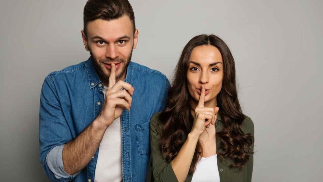 Homem e mulher fazendo gesto de silêncio com o dedo nos lábios
