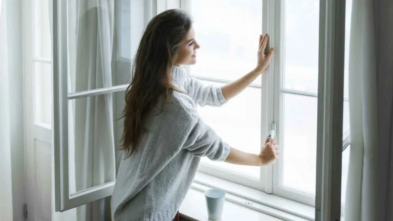 Mulher abrindo janela antirruído em ambiente iluminado e aconchegante, representando ventilação natural e conforto acústico em espaços residenciais.