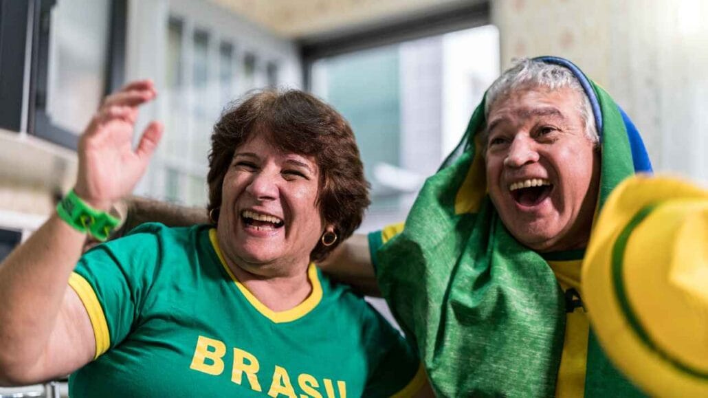 Homem e mulher vestindo roupas nas cores da seleção brasileira comemoram juntos durante um evento esportivo