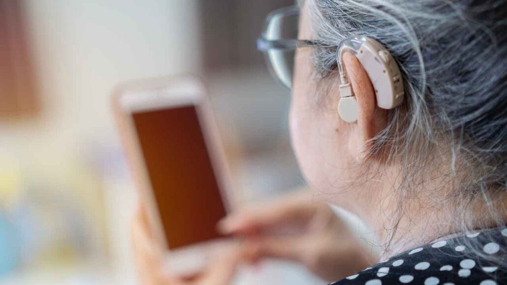 Pessoa idosa usando aparelho auditivo atrás da orelha enquanto segura um smartphone
