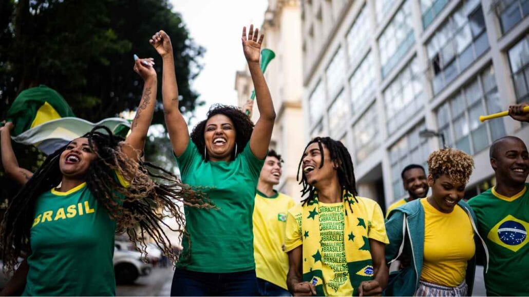 Grupo de torcedores brasileiros vestidos com camisetas verde e amarela celebra em uma rua da cidade