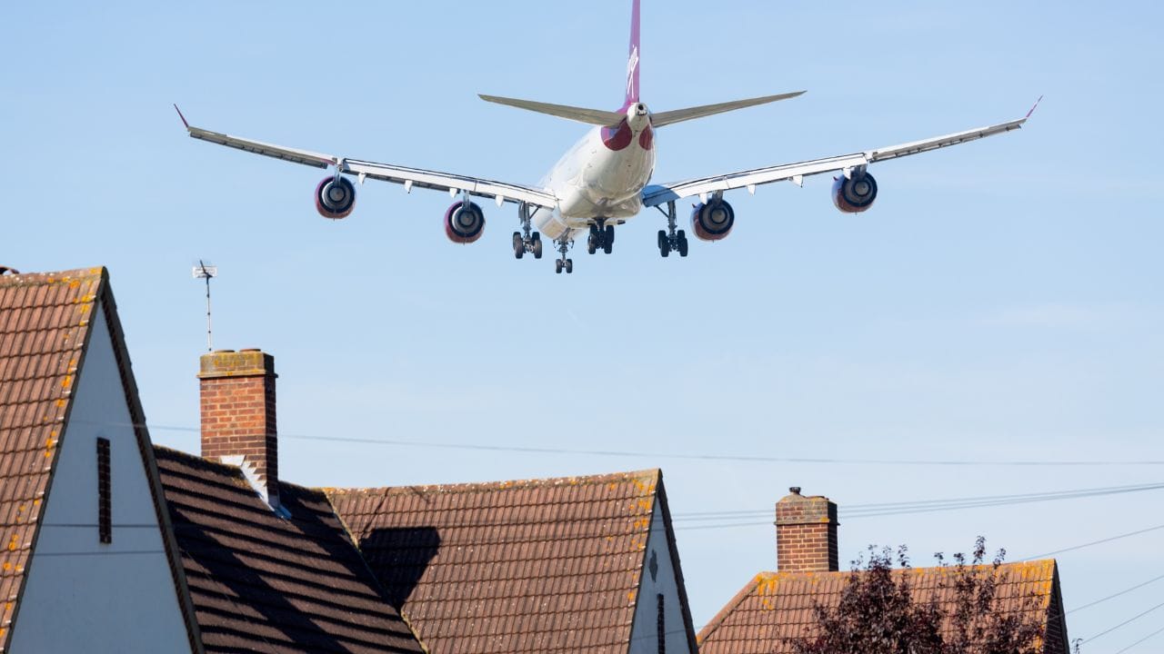 Avião de grande porte sobrevoando uma área residencial em baixa altitude, próximo aos telhados das casas